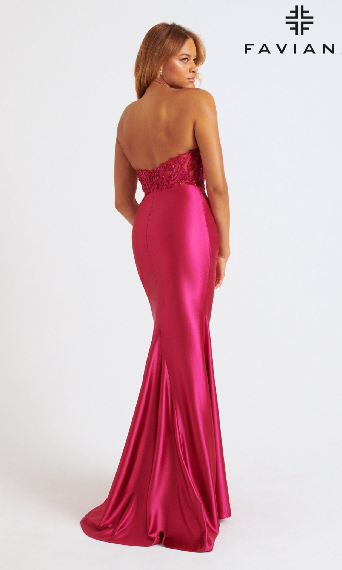 A woman in the Faviana 11246 long prom dress, featuring a strapless satin design with a corset bodice and lace detail, stands facing away. The magenta gown is floor-length, set against a white background with the FAVIAN logo visible.